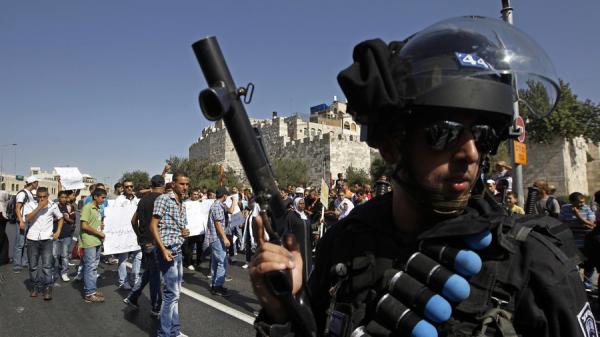 Israeli policemen wearing a belt with rubber bullets stands near Palestinian protesters, 2012