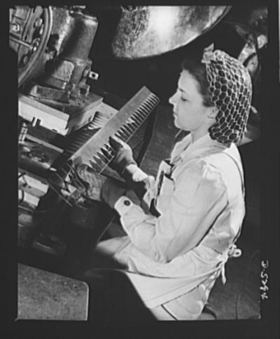 A young woman worker ‎operates a heavy punch-press in a large Western aircraft plant, USA 1942, fotografia di David ‎Bransby, dal database della Library of Congress.‎