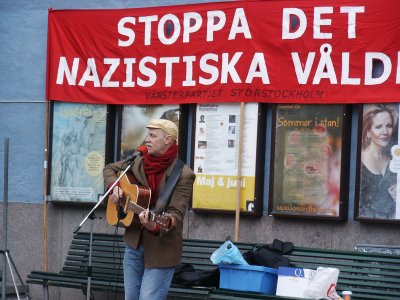 Jan Hammarlund canta nel centro di Stoccolma. Sullo striscione alle sue spalle: "Fermare la violenza nazista".