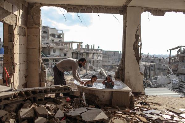 Palestinian father bathing his daughter and niece in their destroyed home.