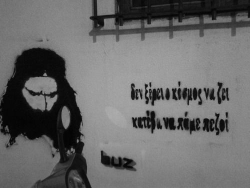 "Il mondo non sa vivere. Scendi e andiamo a piedi". Su un muro con l'immagine stencilata di Nikolas Asimos.